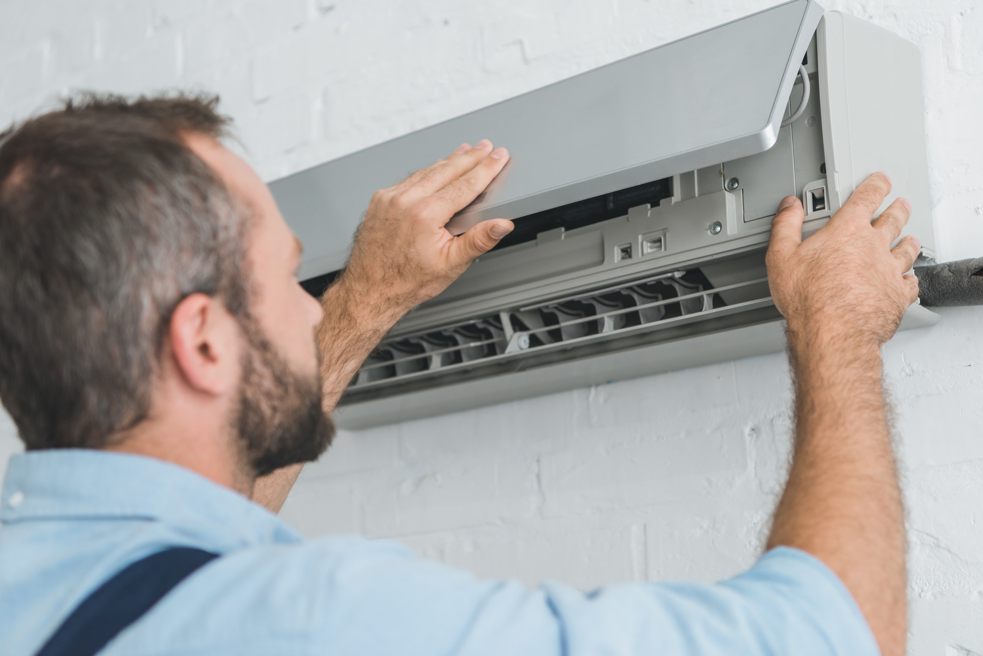 Monteur opent airco-binnenunit voor onderhoud aan filters